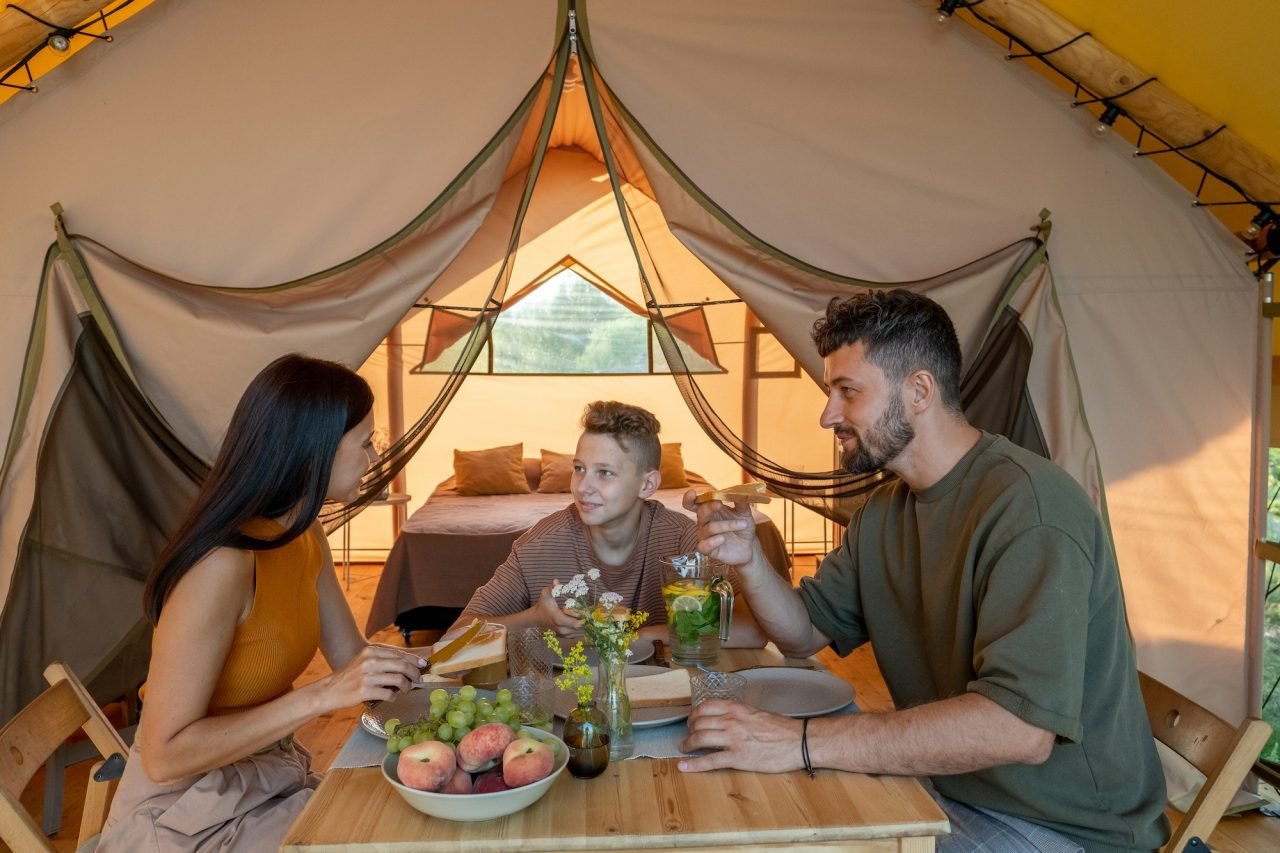 happy young family having breakfast by glamping tent